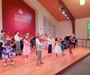 Young violin students performing in a group on stage