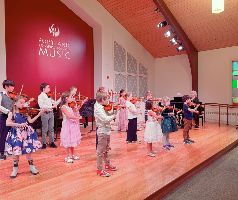 Young violin students performing in a group on stage